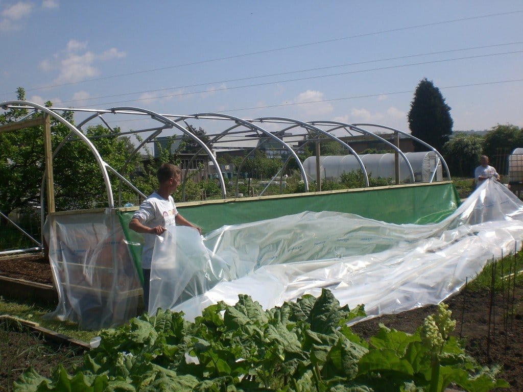 two men adding wind break netting to stop polytunnel blowing away