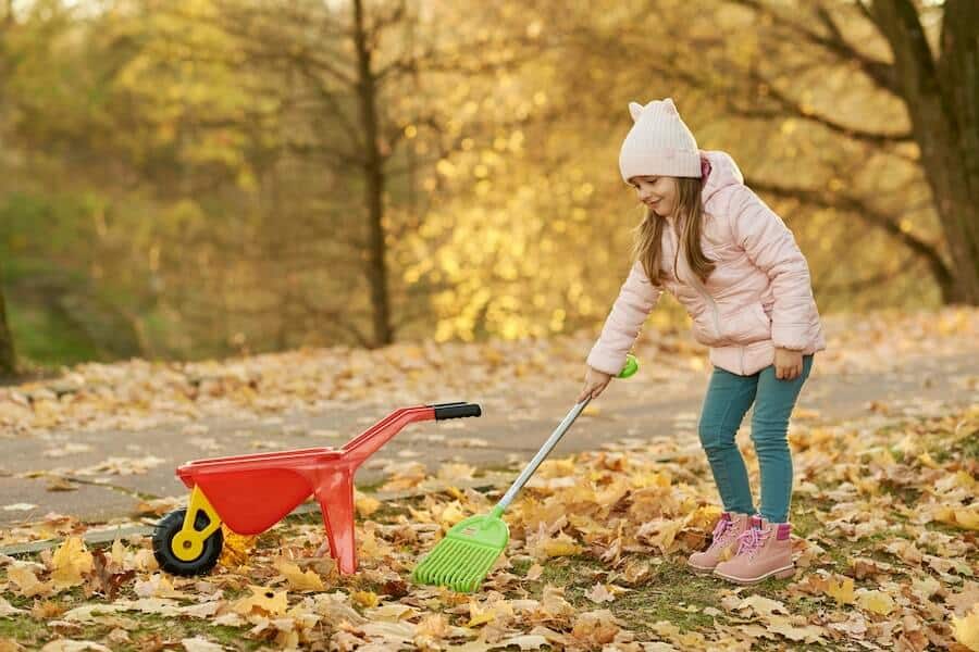 young girl using a leaf rake from an essential garden tools list