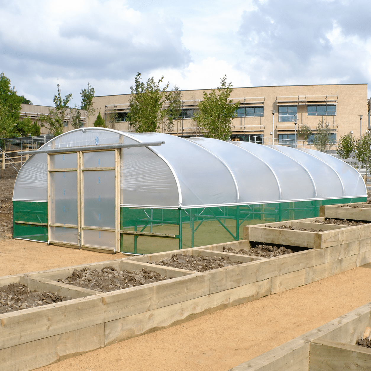 Polytunnel with closed timber sliding double doors, green side netting and raised beds in front